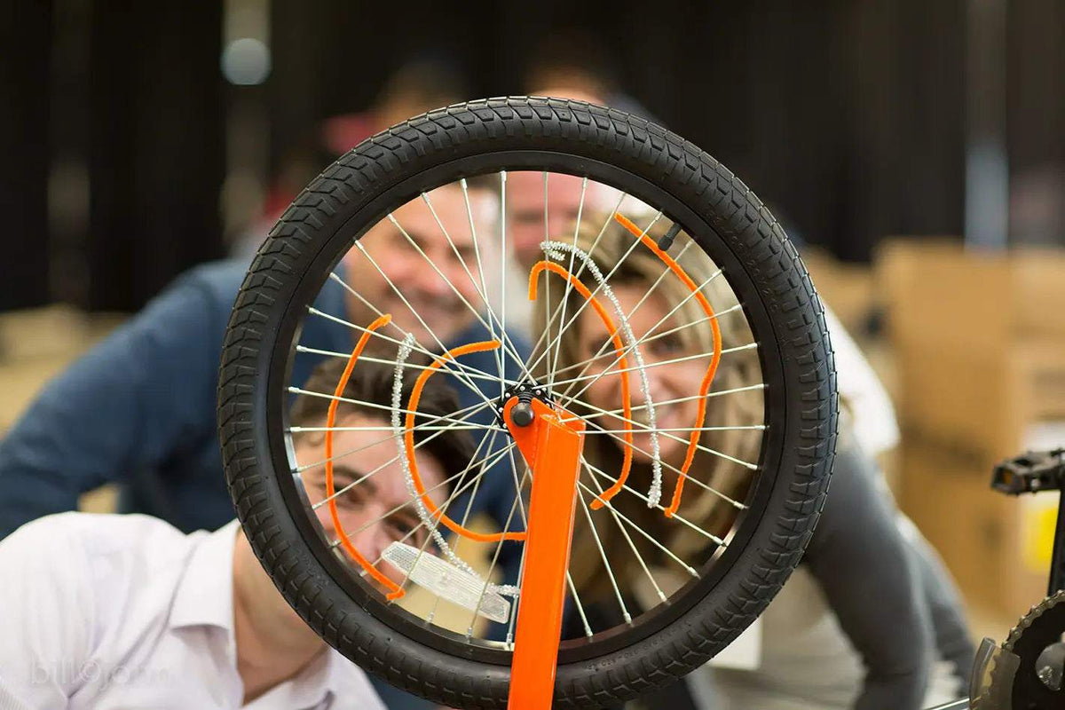 Bicycle wheel with a black rubber tire, silver spokes and bright orange frame, part of team building for large groups.