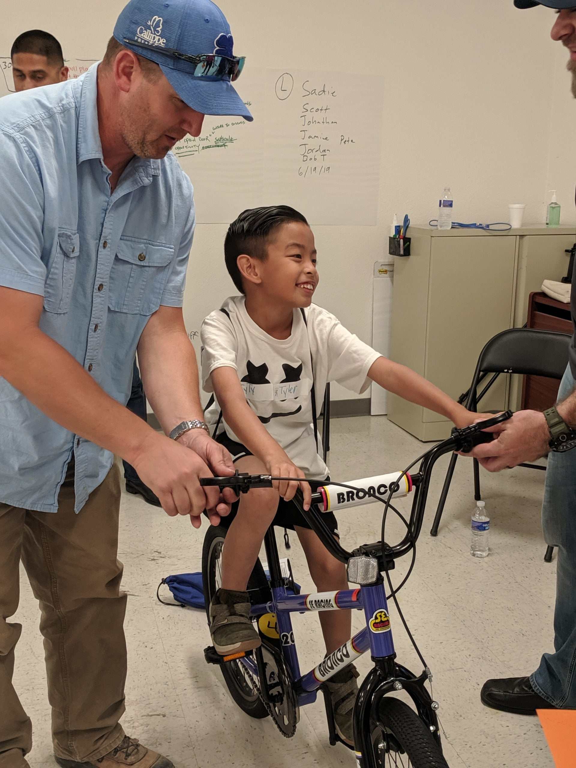 Child riding assembled BMX bike with adult assistance in indoor team building activity using Life Cycles™ Team Building Kit