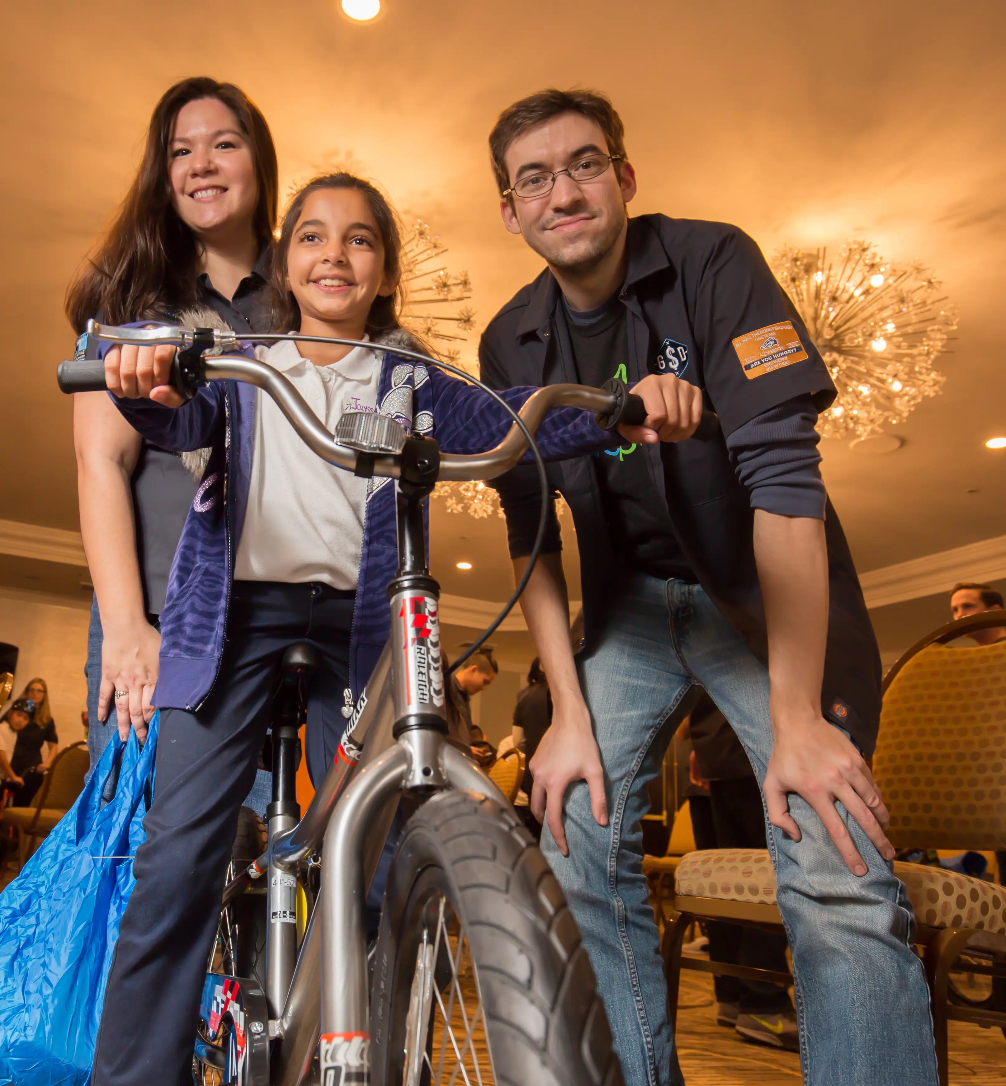 Three people posing with a bicycle indoors, likely in a social setting.