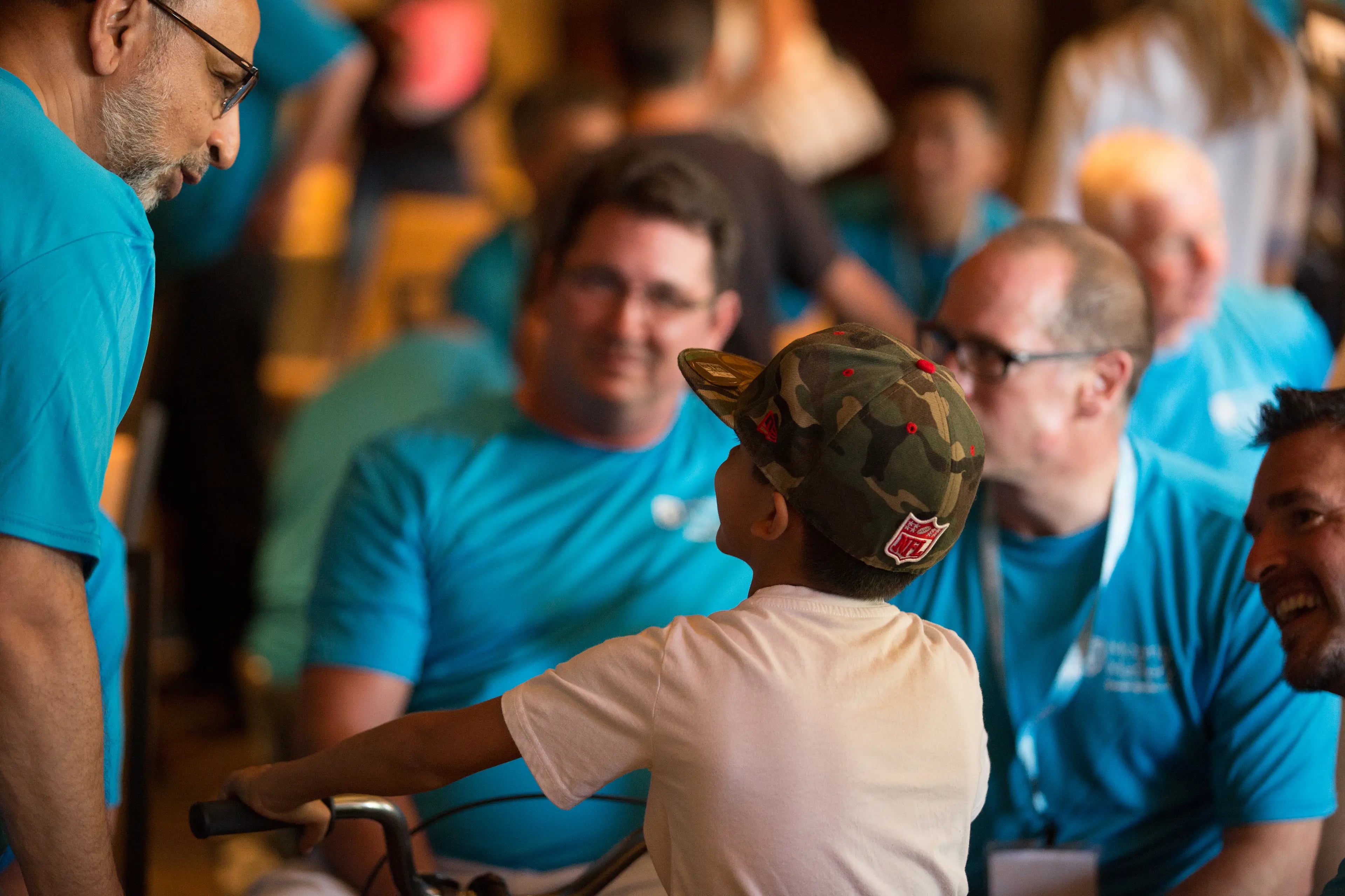 Person wearing a camouflage hat with a logo, surrounded by people in blue shirts.