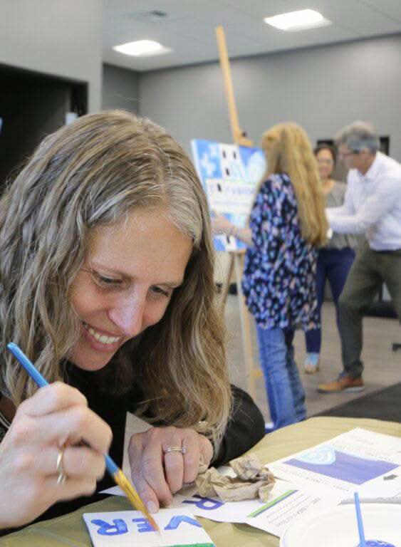 Woman painting a piece of artwork as part of a Team Mosaic™ Kit team building activity with colleagues painting in the background