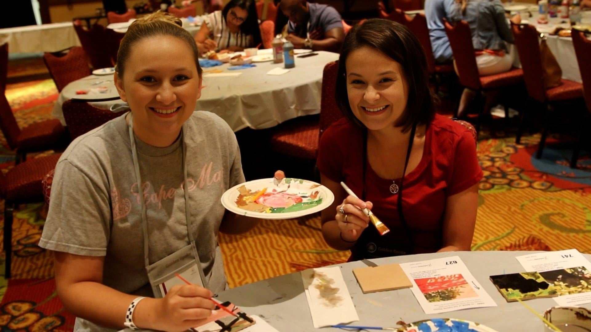 Two women smiling while painting as part of Team Mosaic™ Kit team building activity