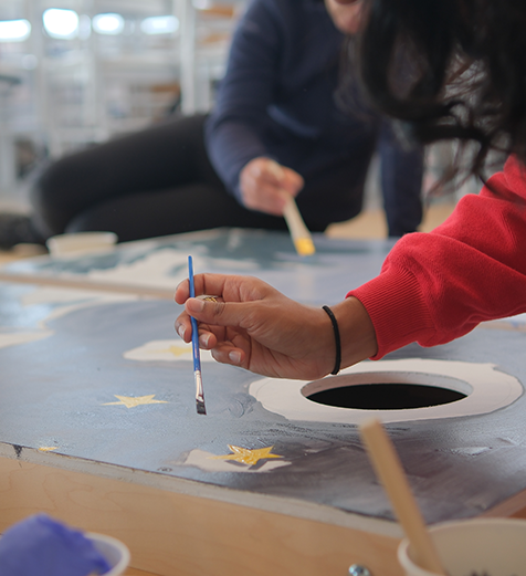 Person painting a star on a canvas with another person in the background.