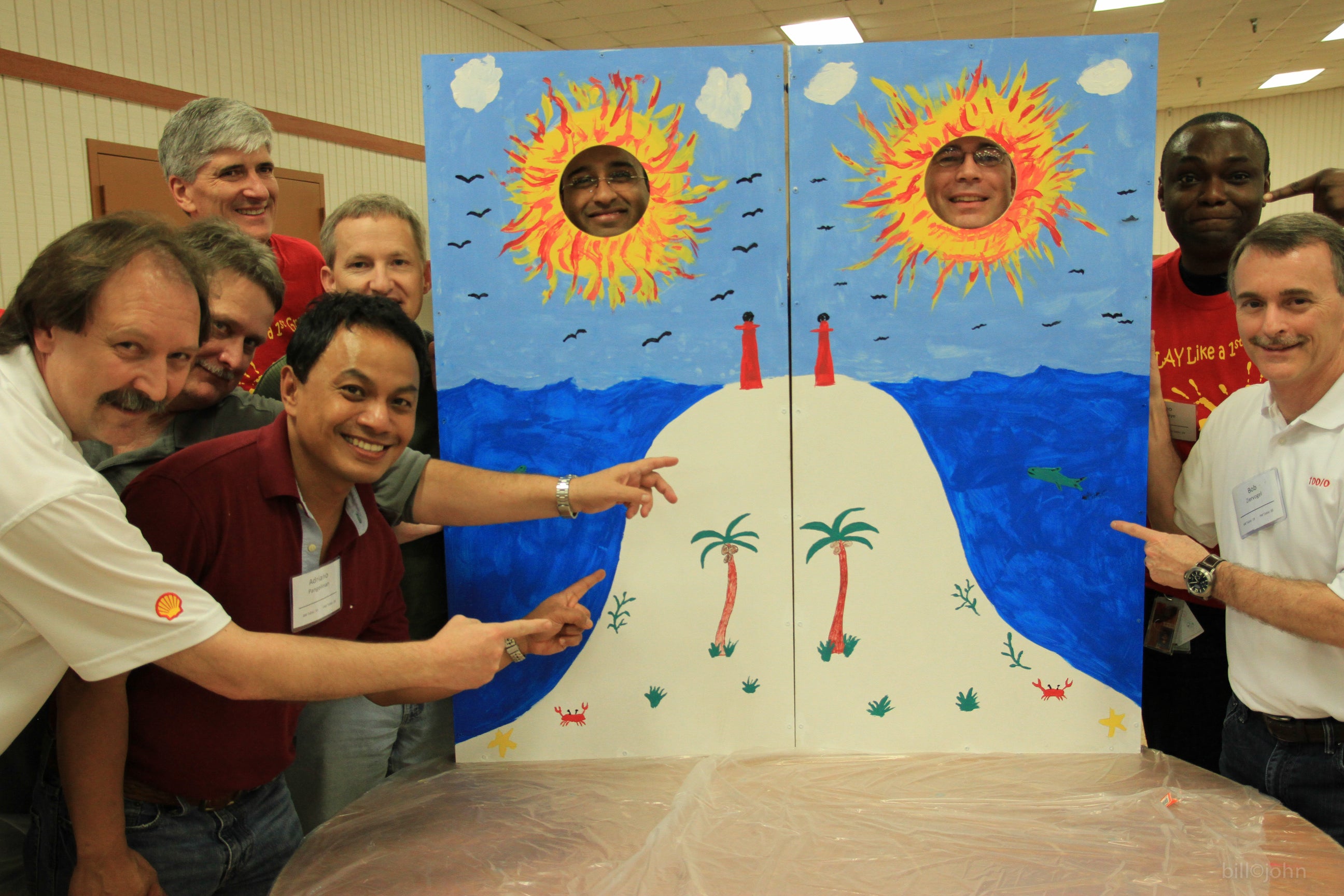 Group of people interacting with a large cardboard cutout of a tropical island with suns on top
