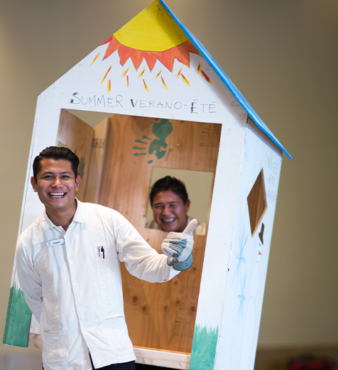 Person posing with a colorful cardboard cutout shaped like a beach hut.