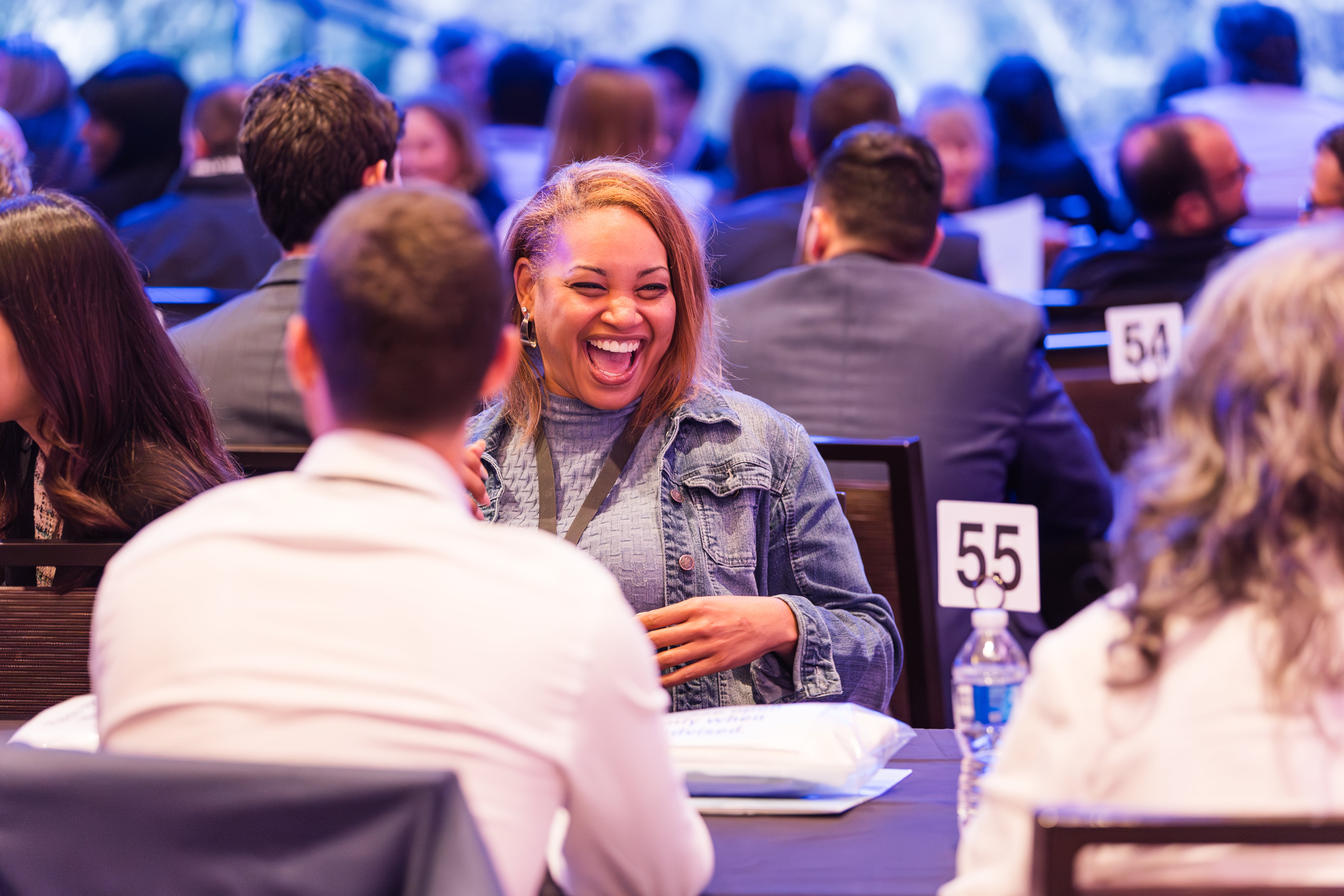 Woman laughing at a Odyssey Teams leadership skills event with people seated around tables.