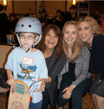 Child wearing helmet and holding painted skateboard deck with three smiling adults during The Board Meeting™ Kit team building event