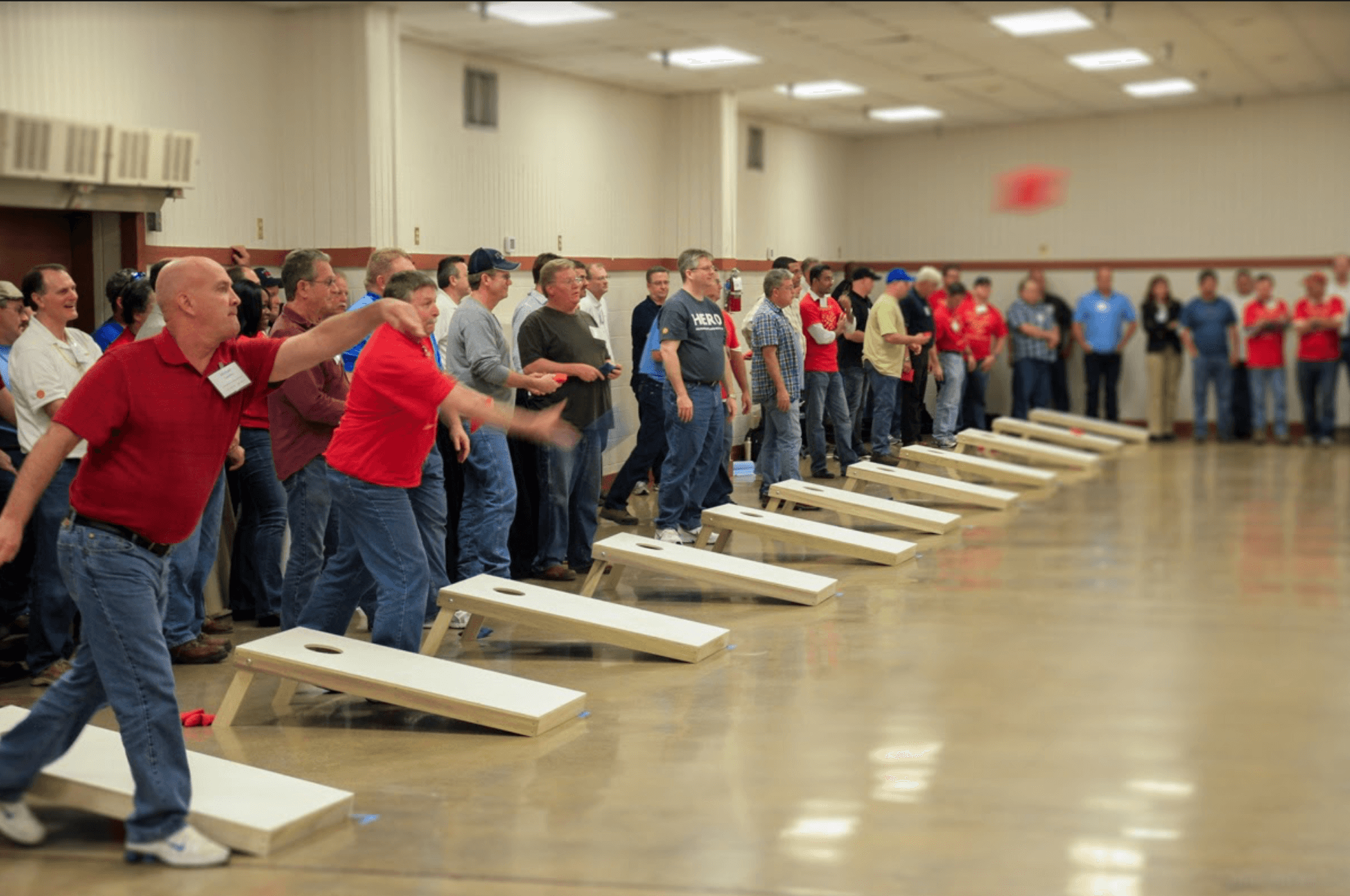 Group of people playing cornhole indoors using Play-it-Forward™ Team Building Kit boards during a tournament