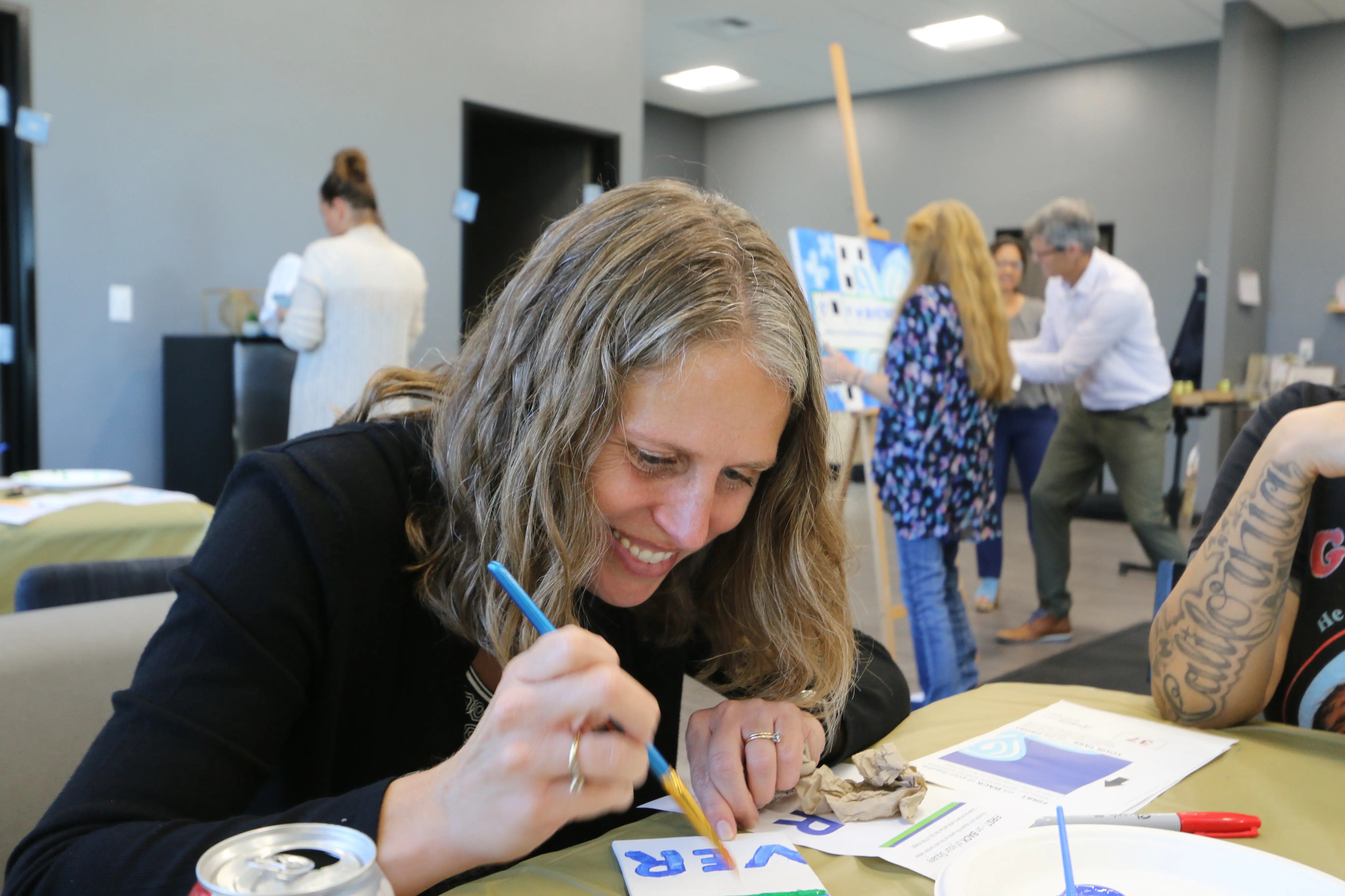 Woman painting at a table with other people in the background