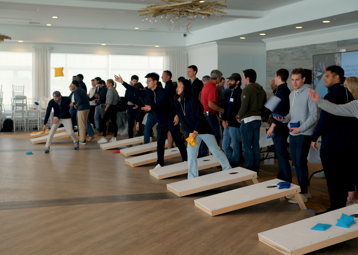 Group of people participating in a team-building activity with corhole games in a room.