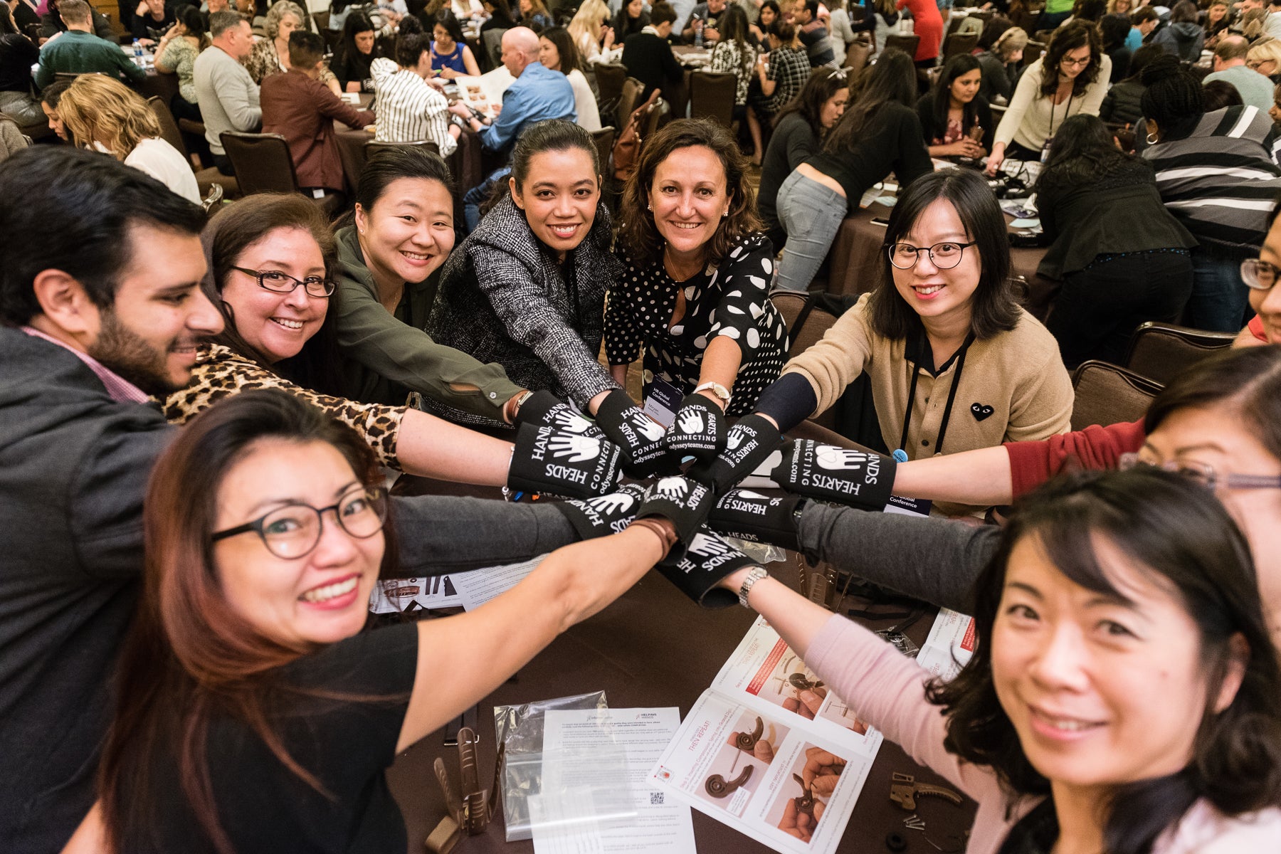 Group of people in a crowded room, likely at an event or gathering, with some wearing gloves.